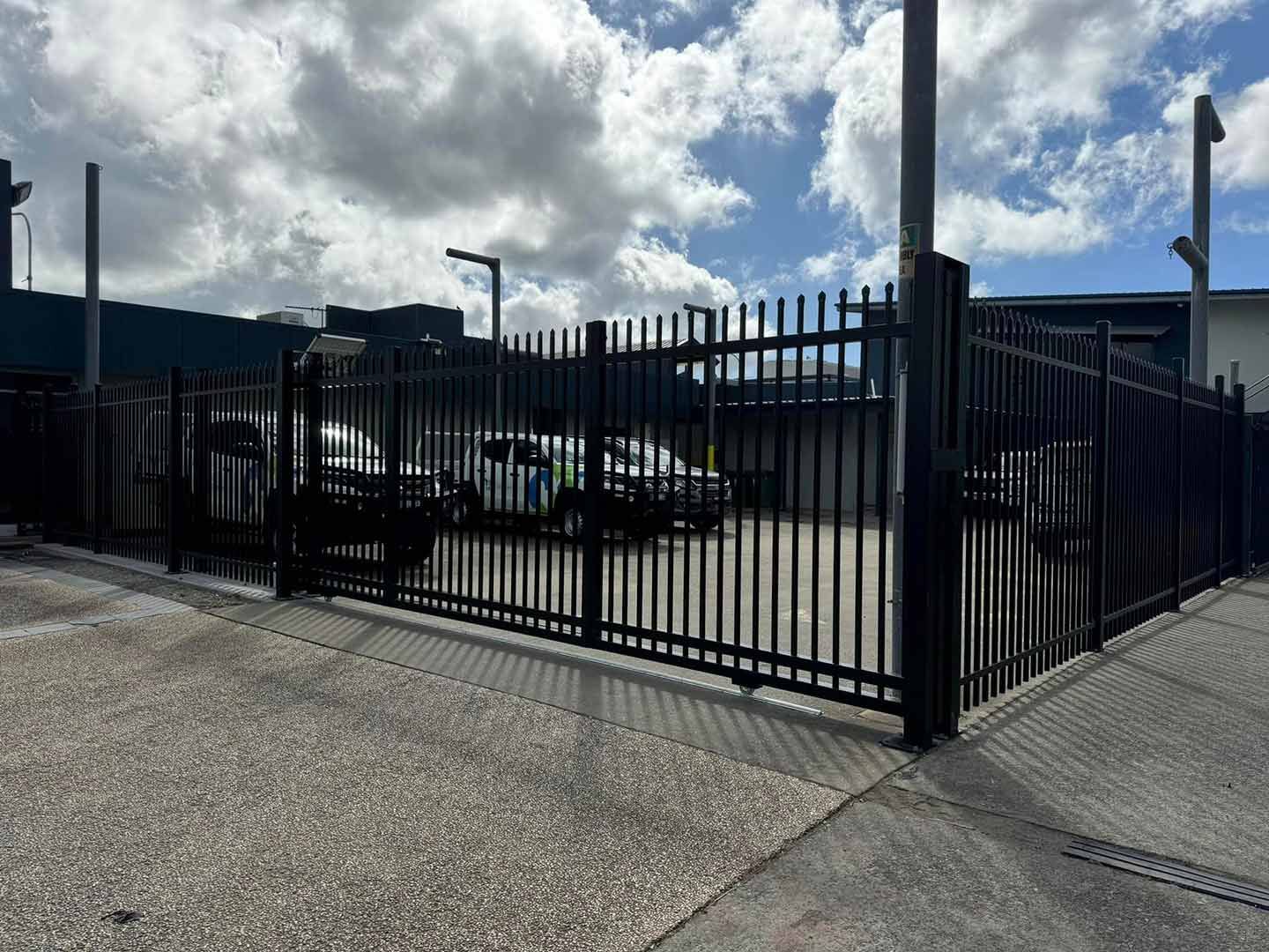 A Black Electric Fence Surrounds A Parking Lot With Cars Parked In It — Dog Gone Fencing in Paget, QLD