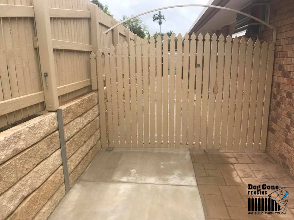 A Wooden Fence Is Surrounding A Brick Wall And A Concrete Patio — Dog Gone Fencing in Paget, QLD