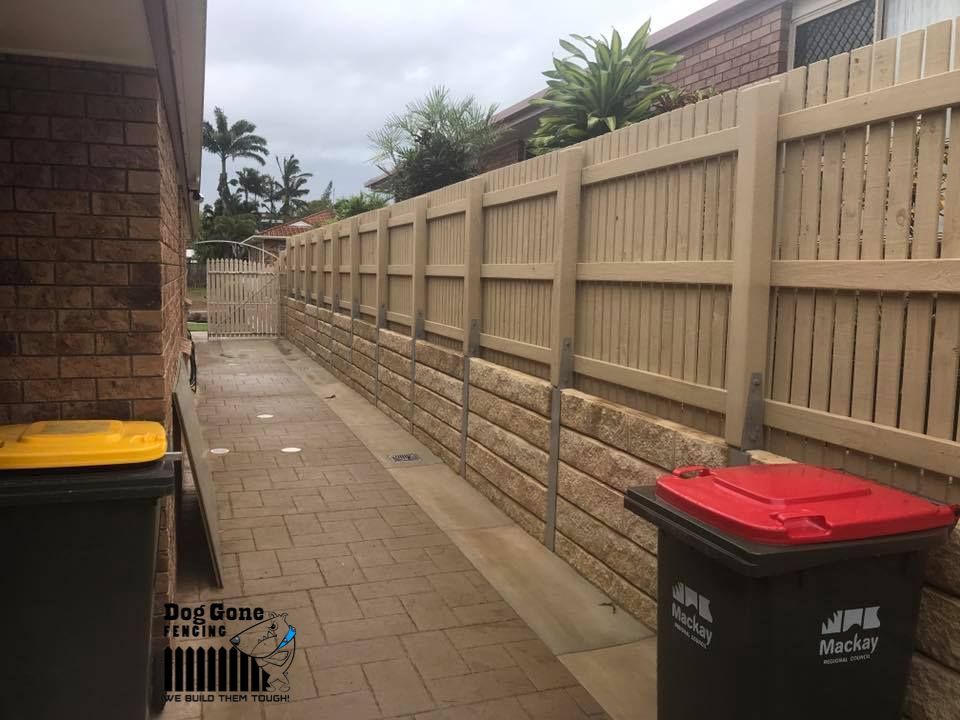 A Brick Wall With A Wooden Fence And Trash Cans In Front Of It — Dog Gone Fencing in Paget, QLD