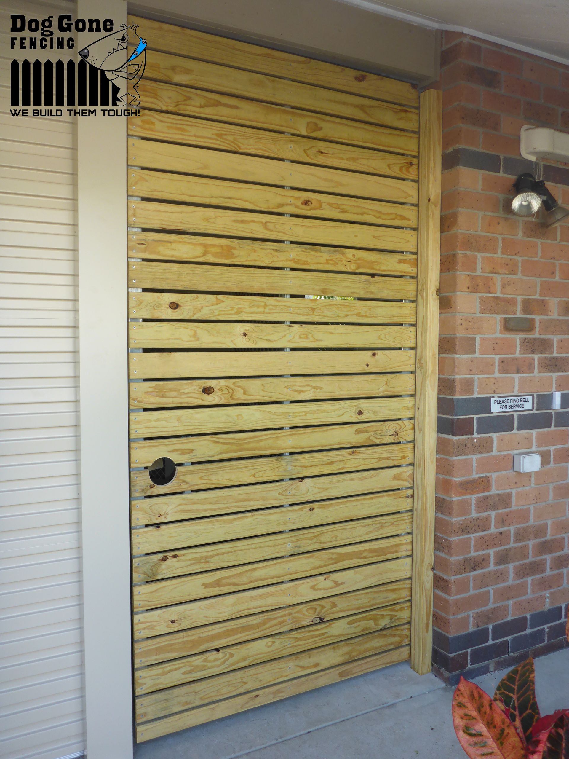 A Wooden Door With A Brick Wall Behind It — Dog Gone Fencing in Paget, QLD