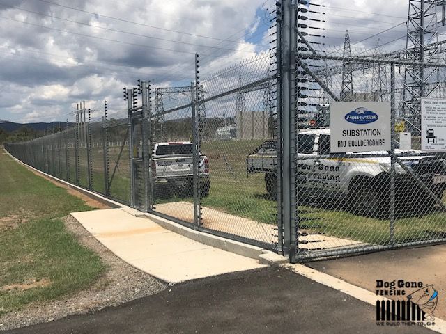 A Chain Link Fence Is Surrounding A Parking Lot With Cars Parked In Front Of It  — Dog Gone Fencing in Paget, QLD