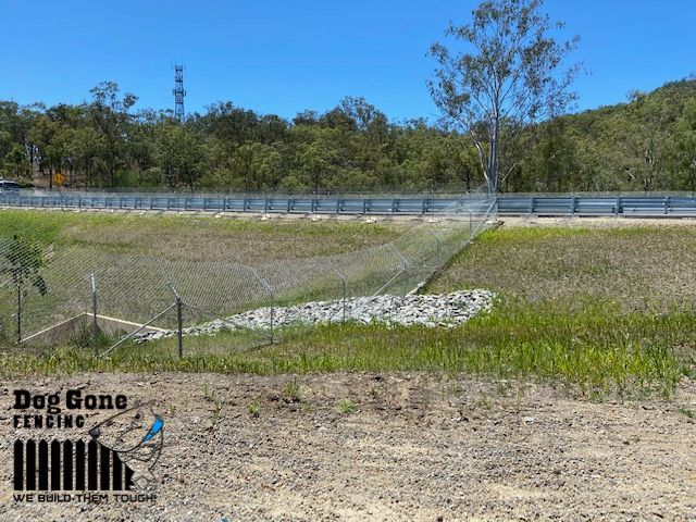 A Fence Surrounds A Grassy Field Next To A Highway  — Dog Gone Fencing in Paget, QLD