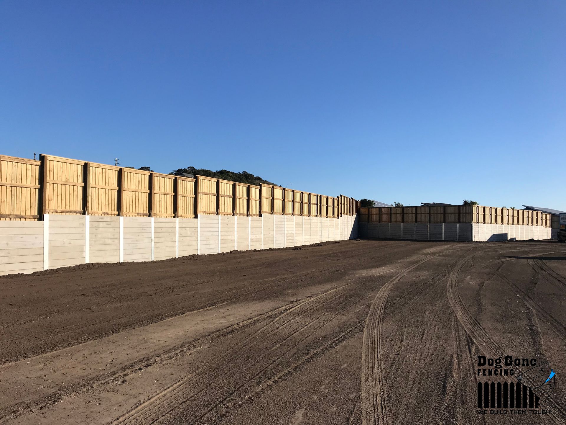 A Large Concrete Wall With Wooden Fences Surrounding A Dirt Road — Dog Gone Fencing in Paget, QLD