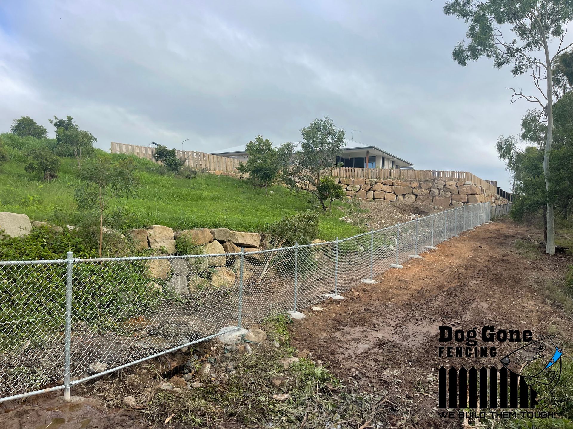 A Dirt Road Next To A Fence With A House On Top Of It — Dog Gone Fencing in Paget, QLD
