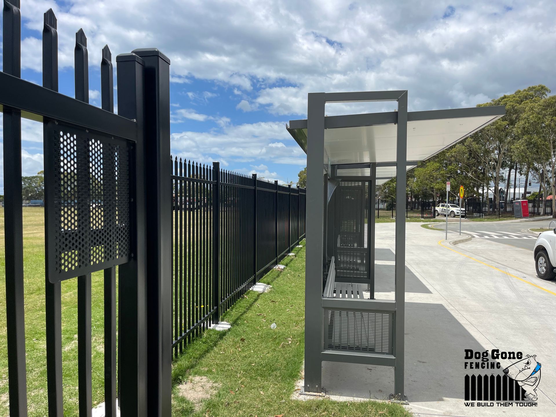 A Black Metal Fence Surrounds A Bus Stop In A Parking Lot — Dog Gone Fencing in Paget, QLD