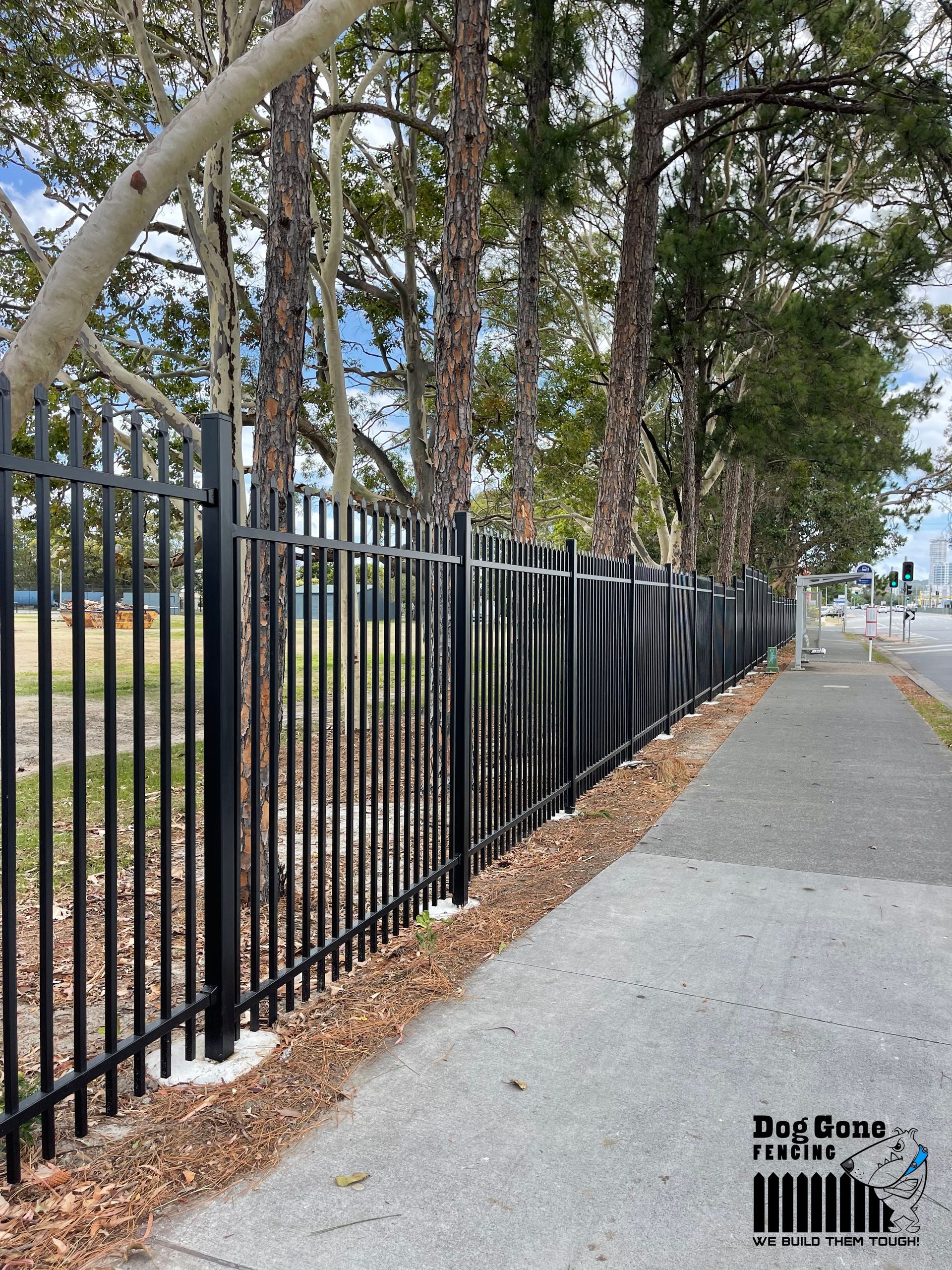 A Black Metal Fence Along A Sidewalk With Trees In The Background — Dog Gone Fencing in Paget, QLD