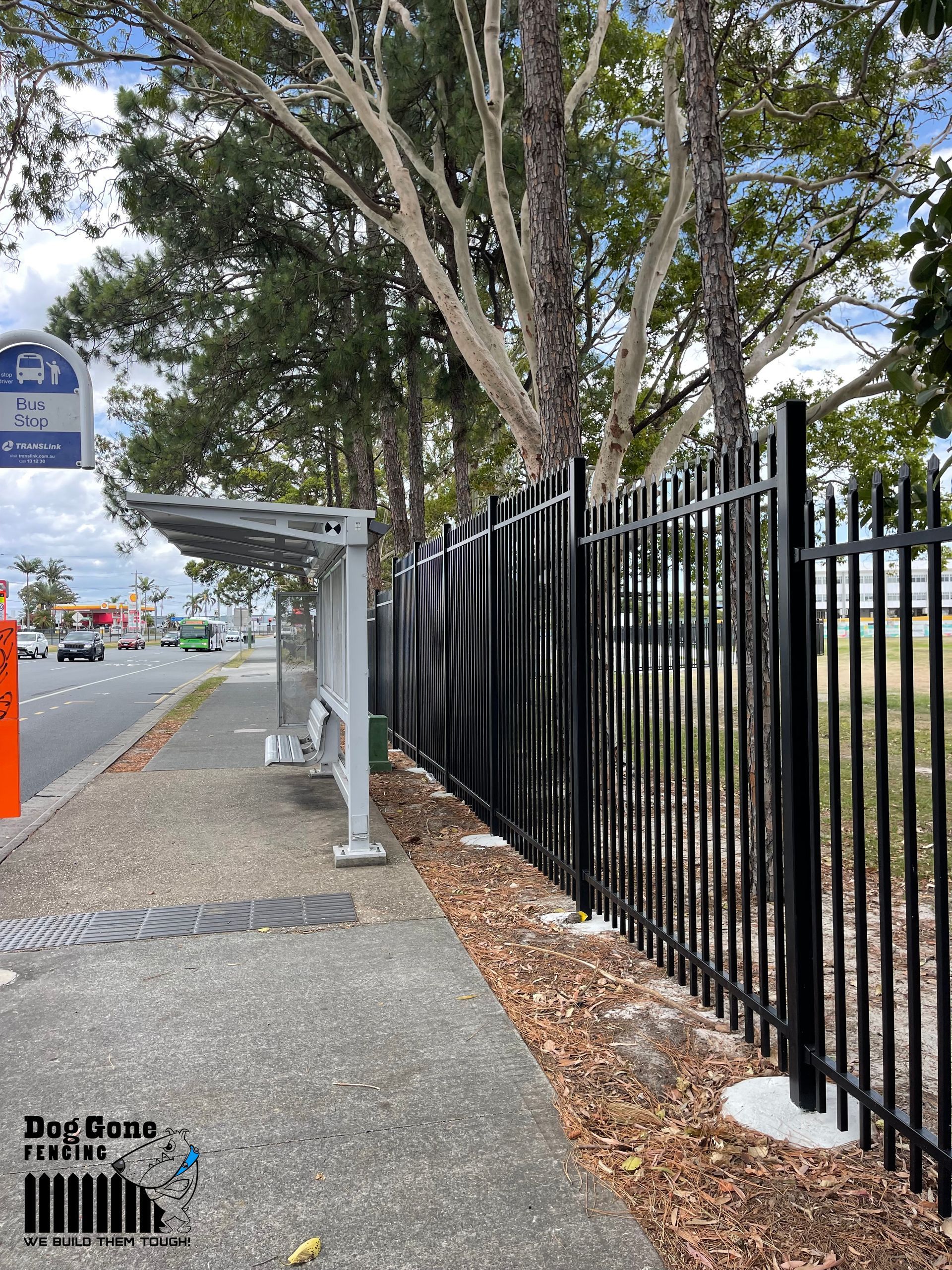 A Black Fence Surrounds A Bus Stop On The Side Of The Road — Dog Gone Fencing in Paget, QLD