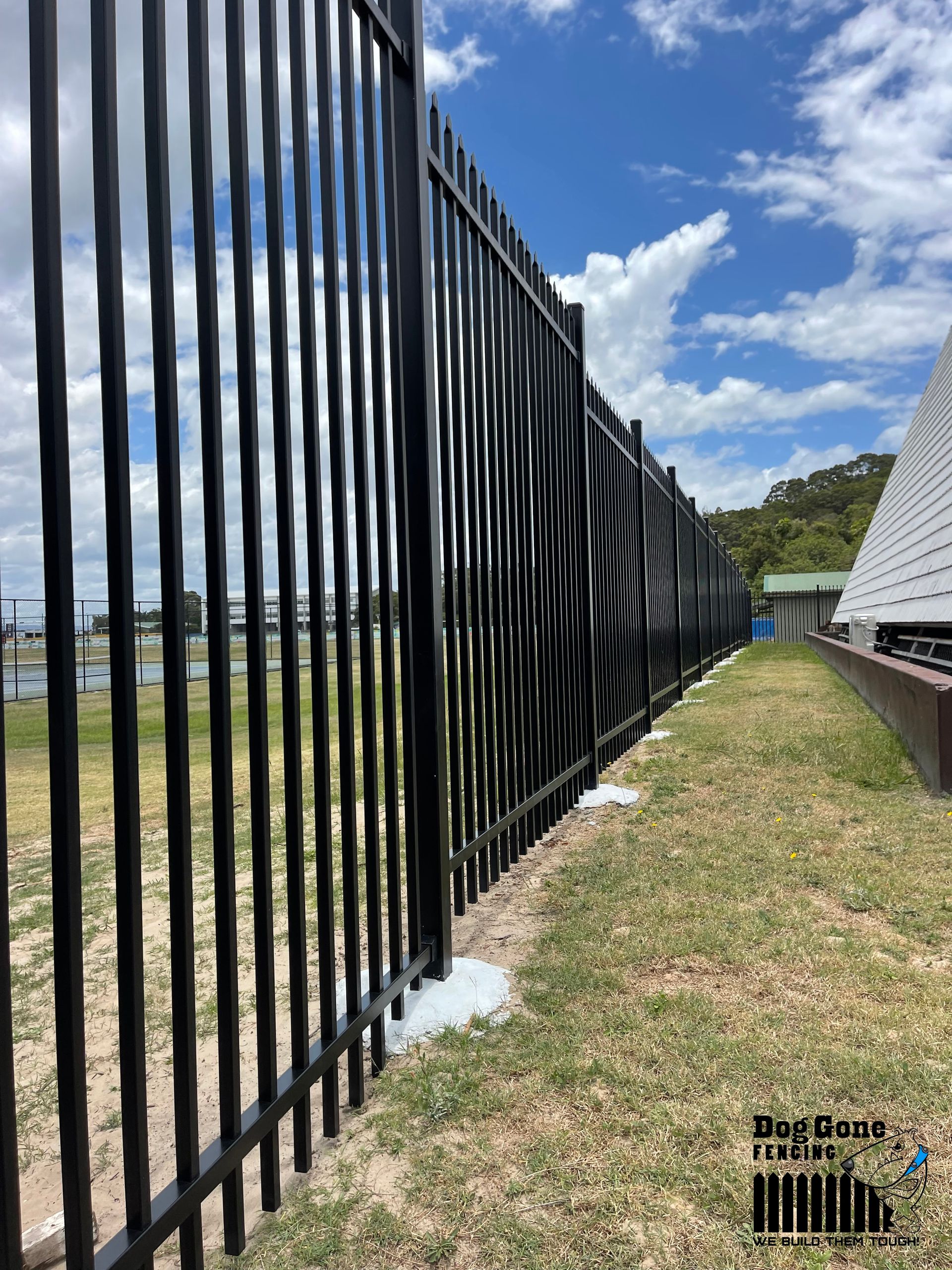 A Black Metal Fence Is Sitting On Top Of A Lush Green Field — Dog Gone Fencing in Paget, QLD