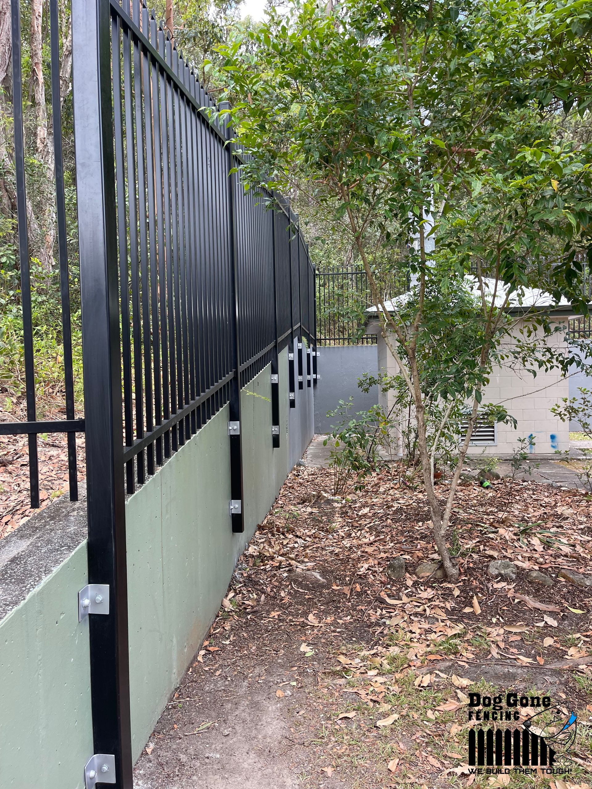 A Black Metal Fence Is Surrounded By Trees And Leaves — Dog Gone Fencing in Paget, QLD