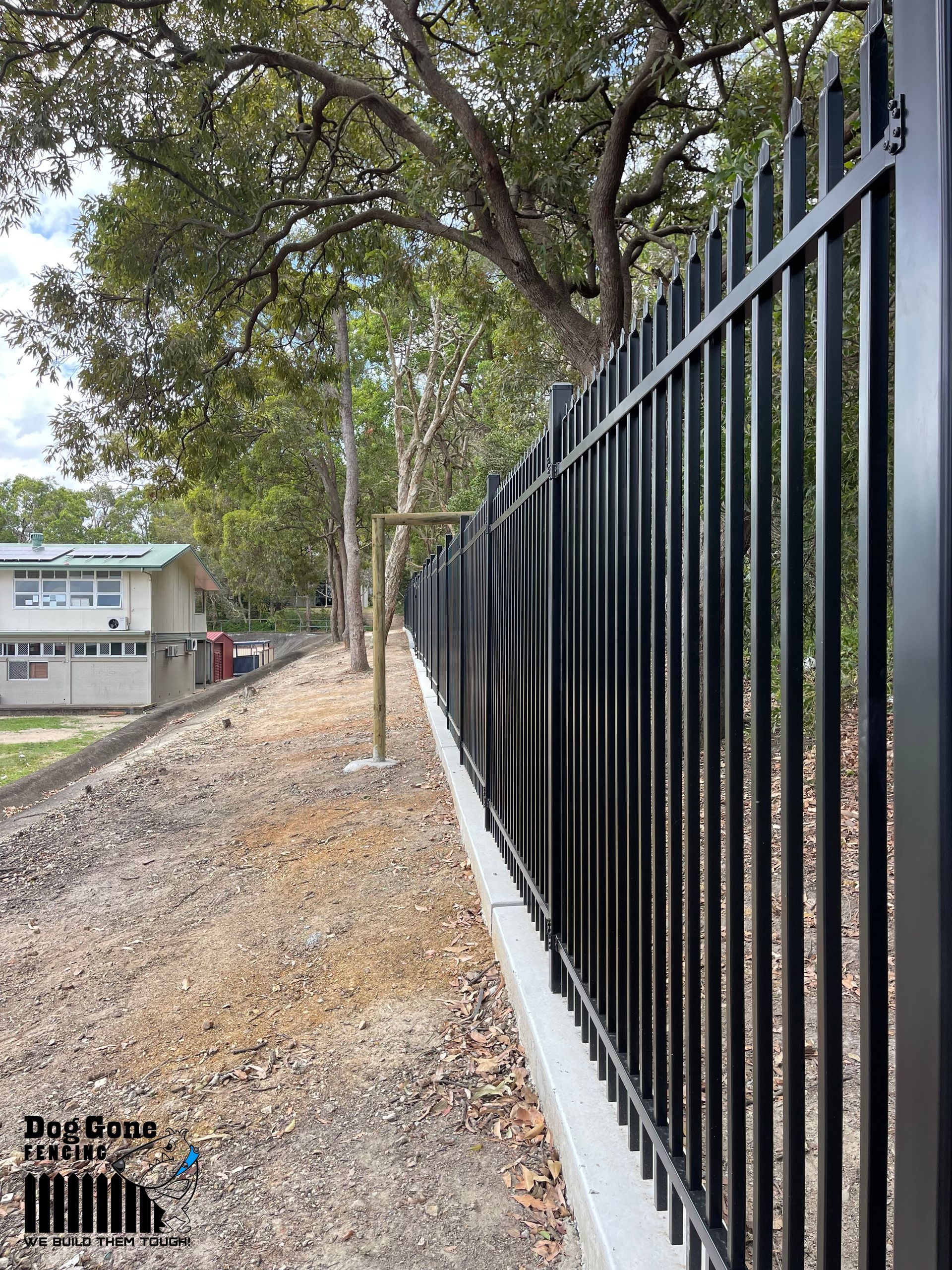 A Black Metal Fence Is Surrounded By Trees And Dirt — Dog Gone Fencing in Paget, QLD