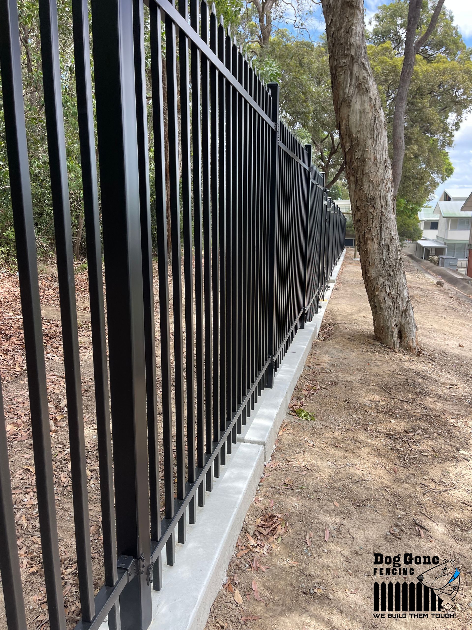 A Black Metal Fence Is Surrounded By Trees And Dirt — Dog Gone Fencing in Paget, QLD