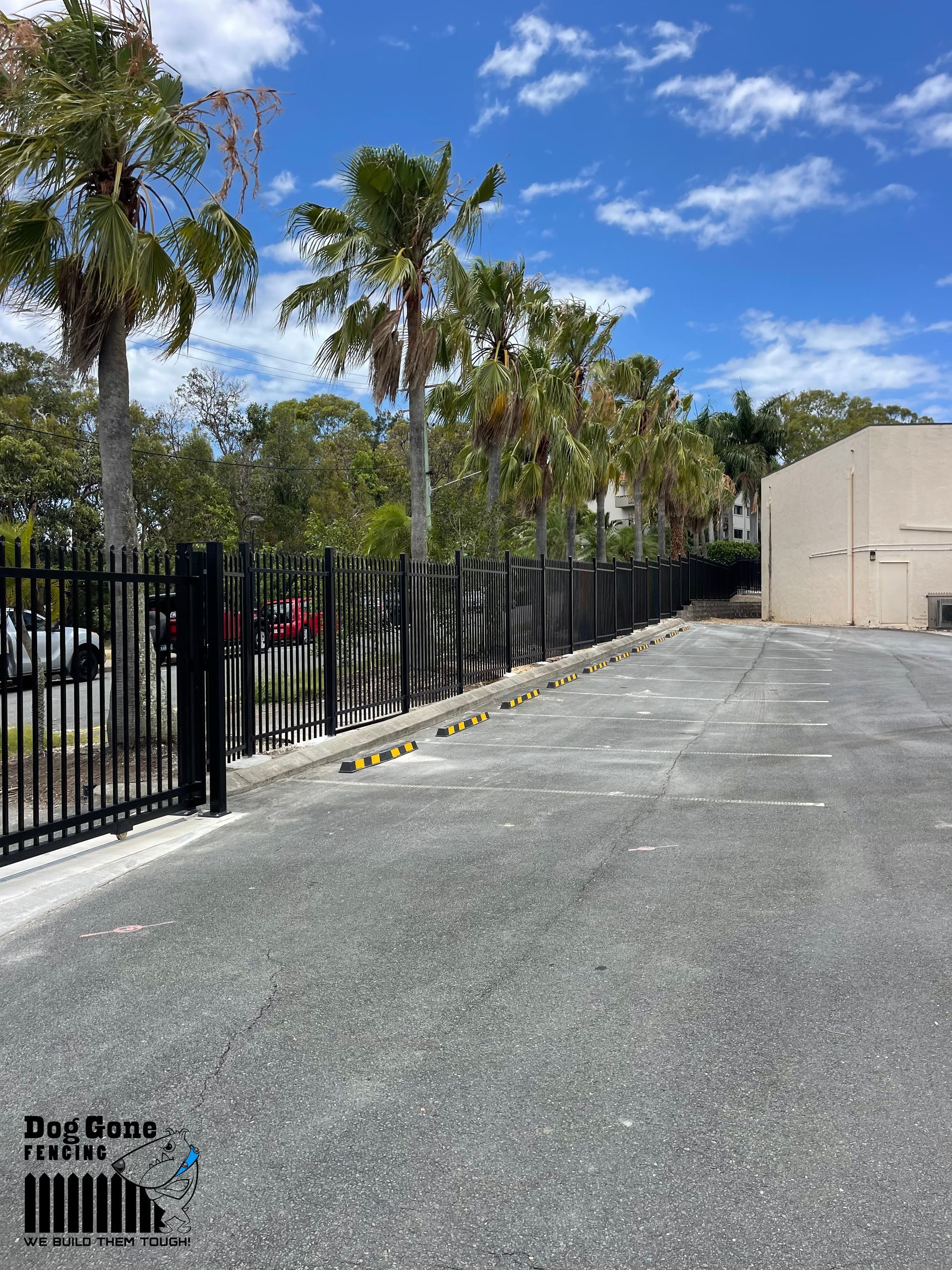 A Fence Surrounds A Parking Lot With Palm Trees And A Building In The Background — Dog Gone Fencing in Paget, QLD