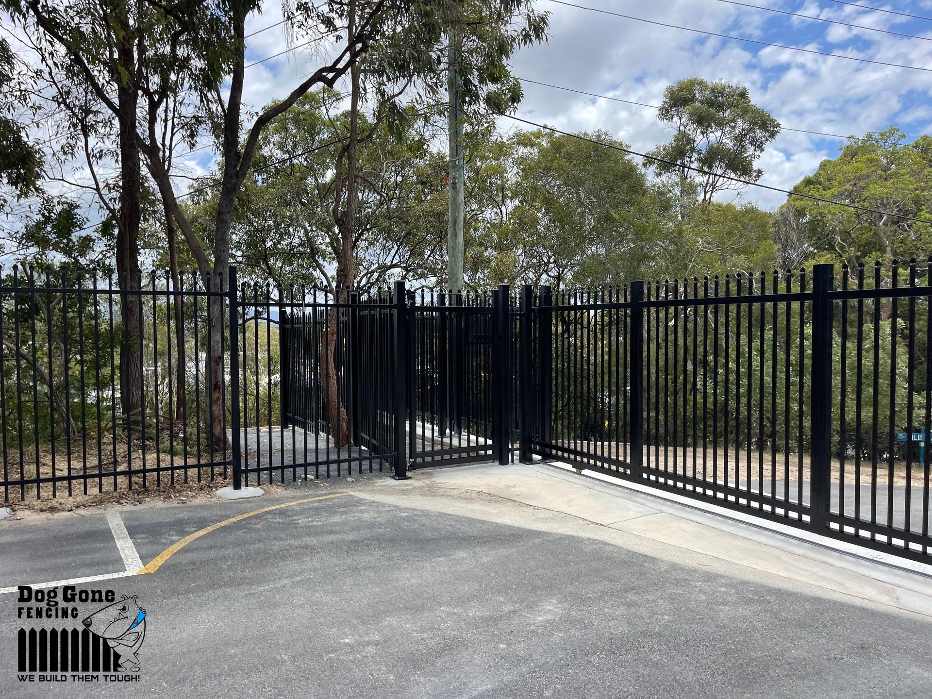 A Black Fence Is Surrounding A Parking Lot With Trees In The Background — Dog Gone Fencing in Paget, QLD