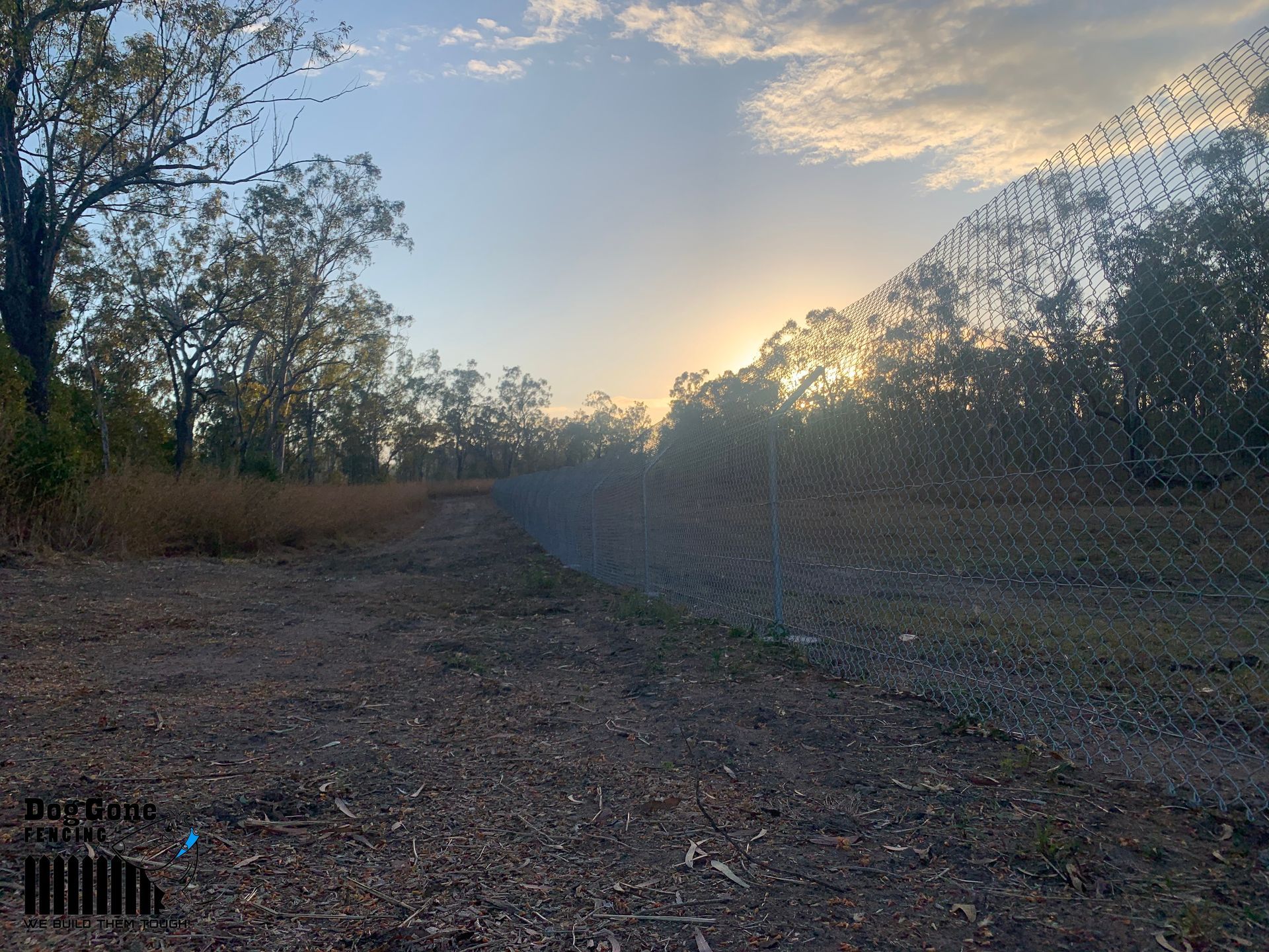 The Sun Is Setting Behind A Chain Link Fence — Dog Gone Fencing in Paget, QLD