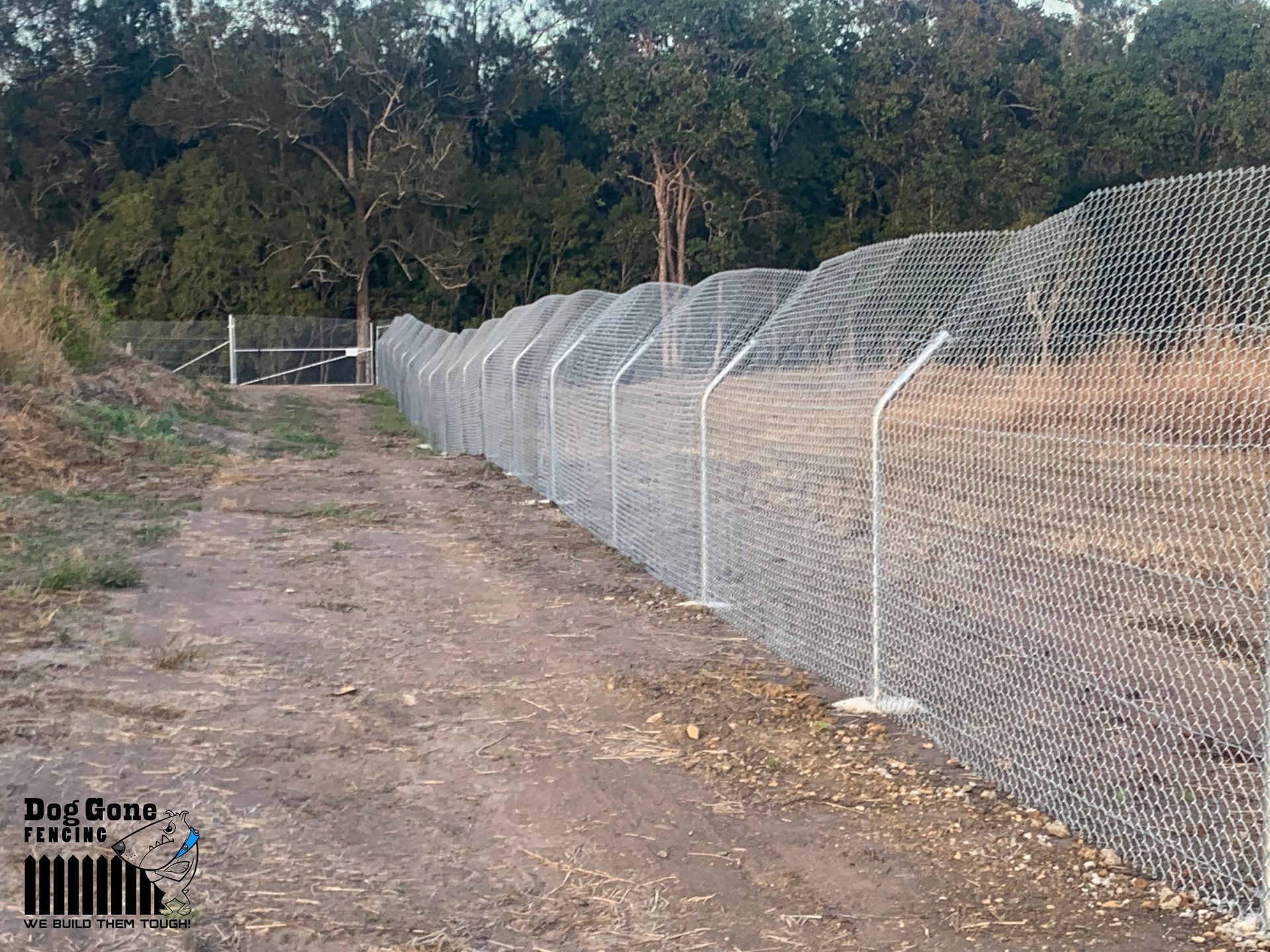 A Chain Link Fence Along A Dirt Road With Trees In The Background — Dog Gone Fencing in Paget, QLD