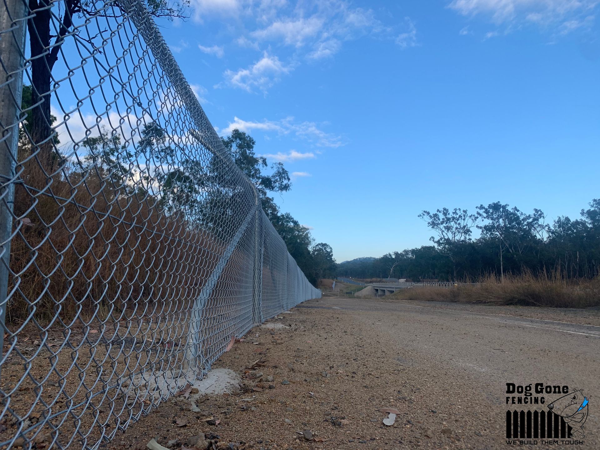 A Chain Link Fence Is Along The Side Of A Dirt Road — Dog Gone Fencing in Paget, QLD
