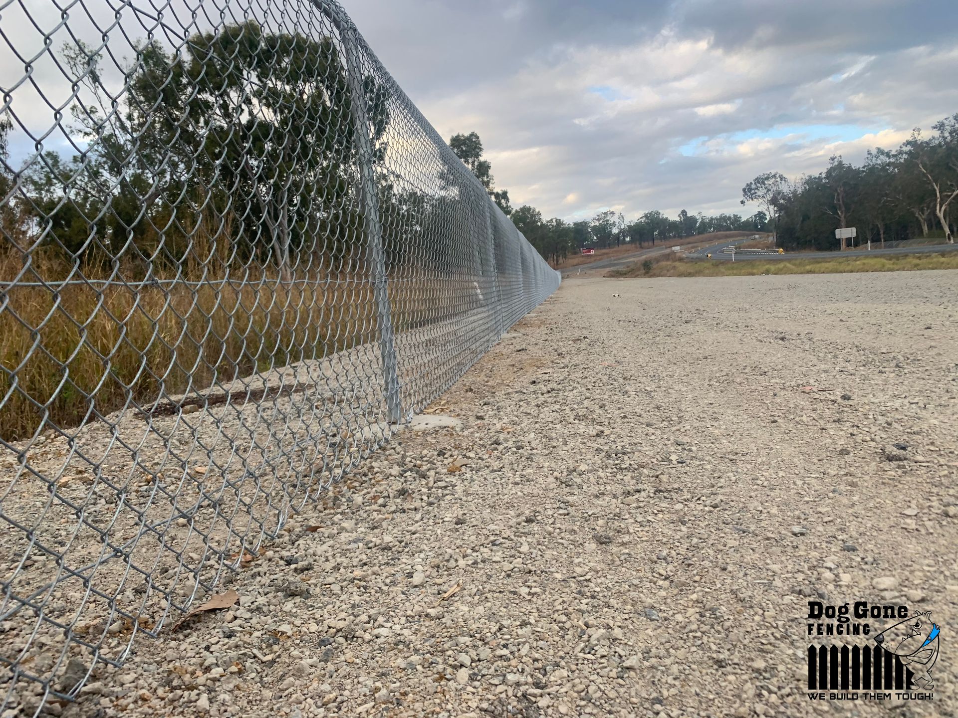 A Chain Link Fence Surrounds A Gravel Area With Trees In The Background — Dog Gone Fencing in Paget, QLD