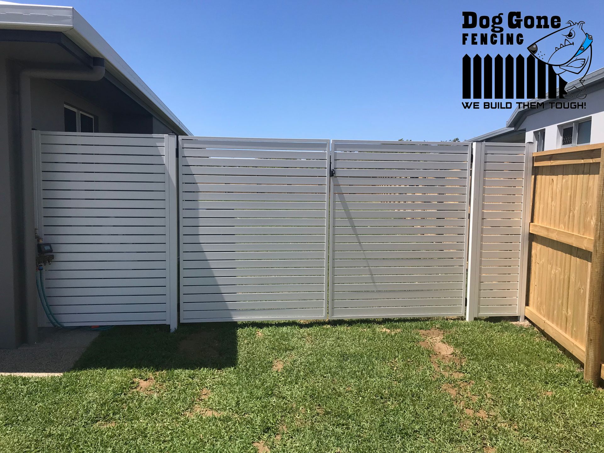 A White Fence With A Wooden Fence In Front Of A House — Dog Gone Fencing in Paget, QLD