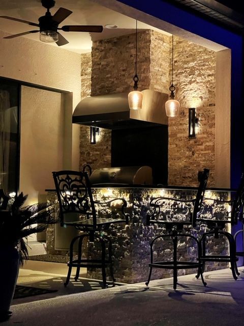 Dimly lit patio dining area with wrought-iron chairs, glass table, and stone wall under pendant lights