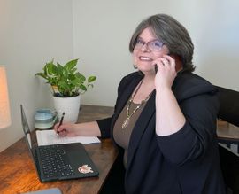 A woman is sitting at a desk talking on a cell phone.