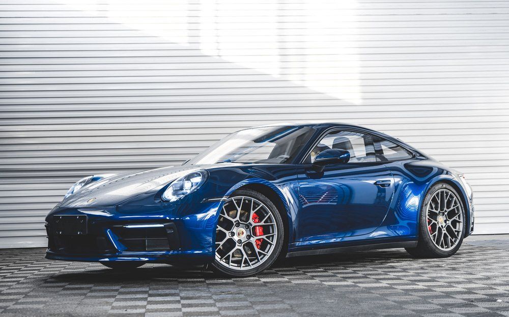 Blue Porsche 911 sports car parked, set against a white-paneled wall, dark wheels, and red brake calipers.
