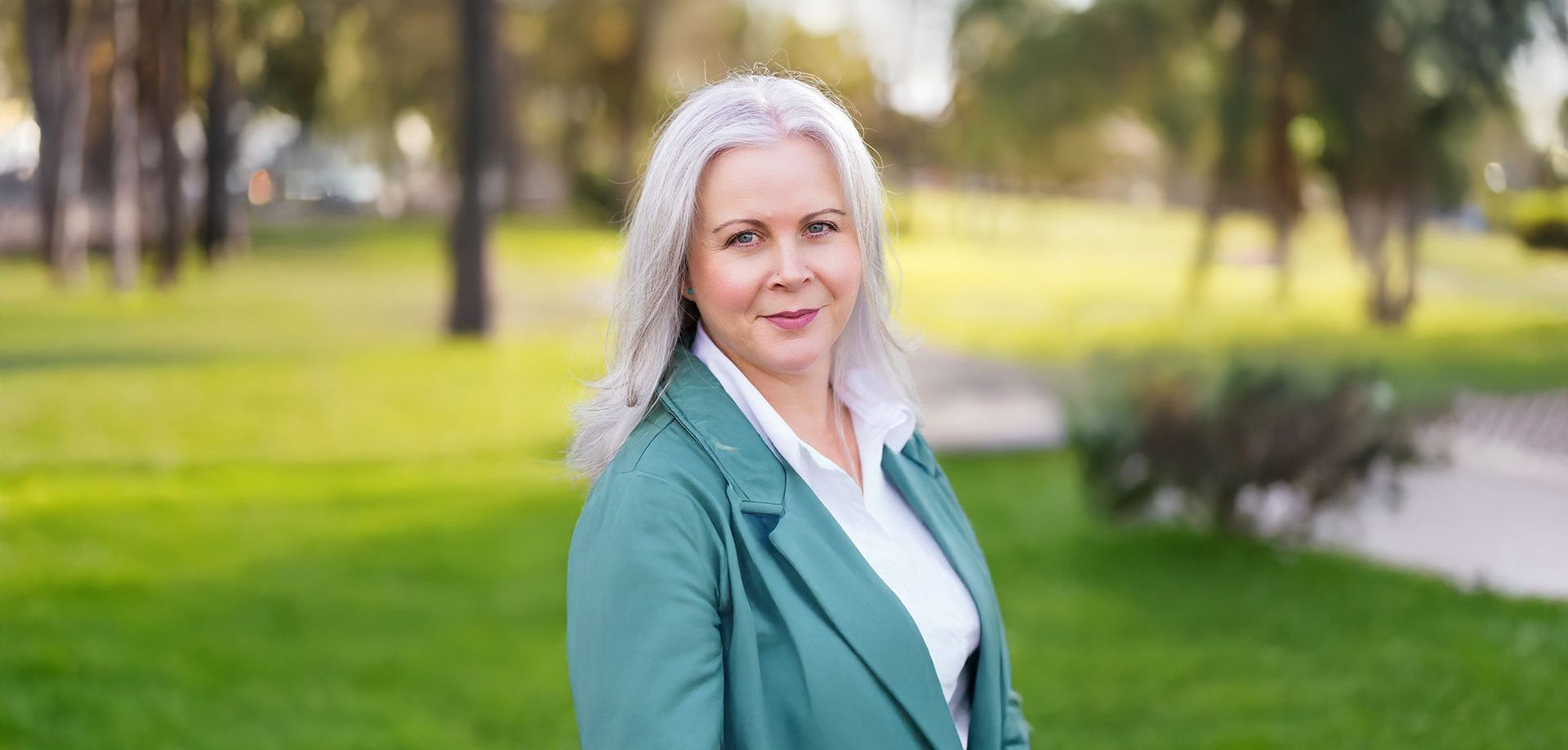 A woman in a black jacket is standing in front of a tree.