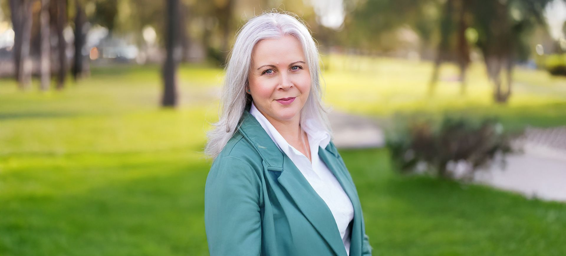 A woman in a black jacket is standing in front of a tree.