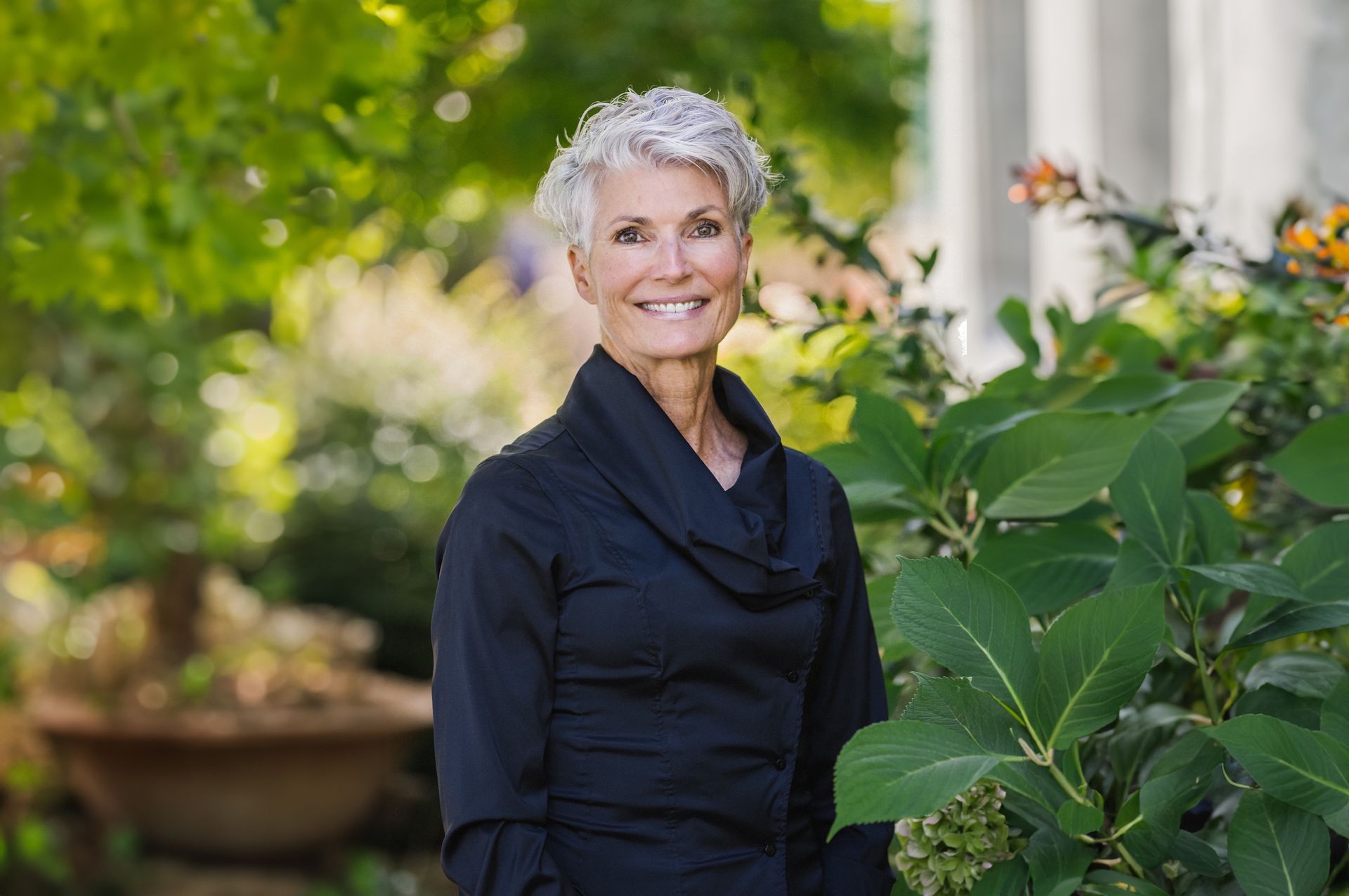 A woman in a black shirt is standing next to a plant and smiling.