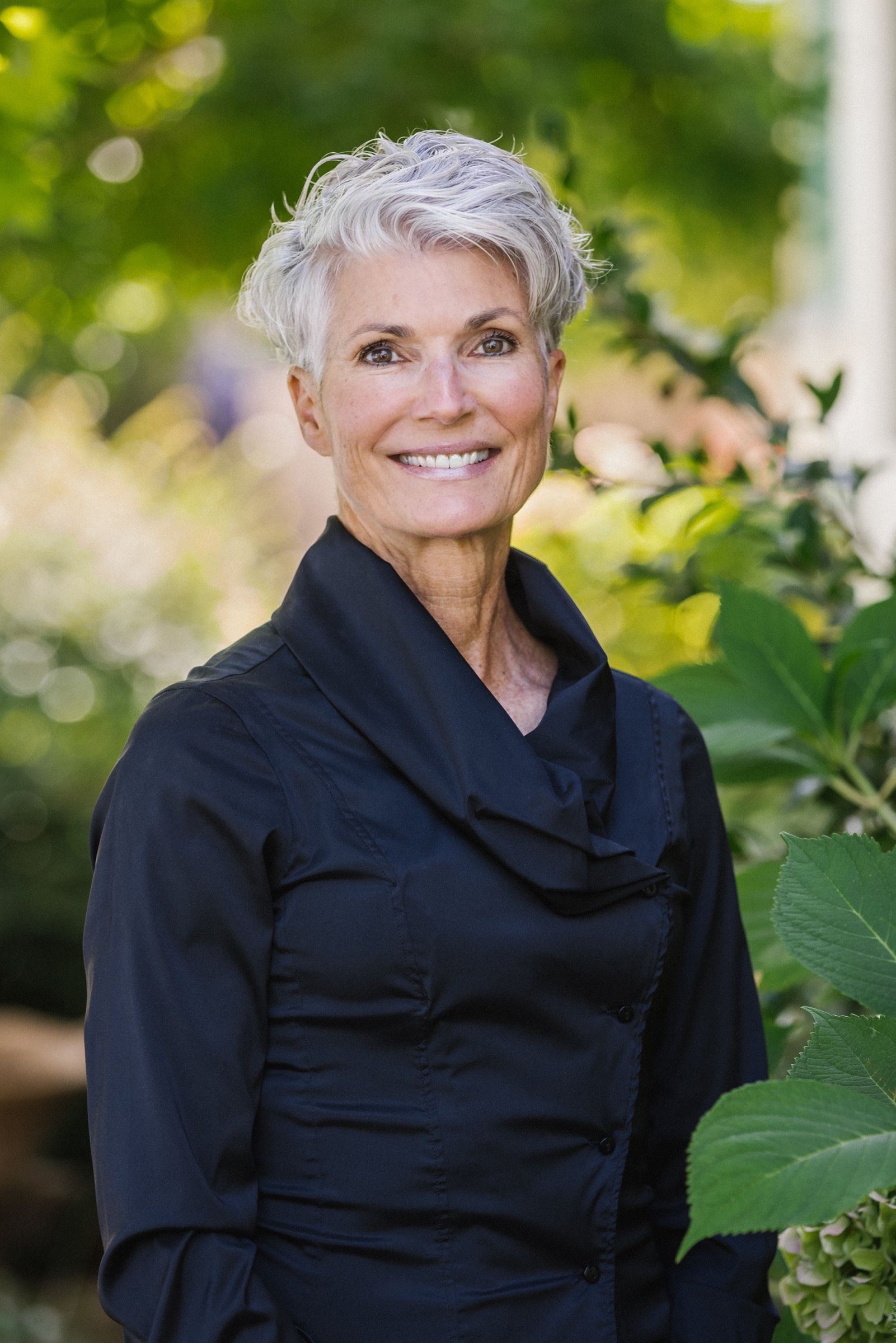 A woman with gray hair is wearing a black shirt and smiling.