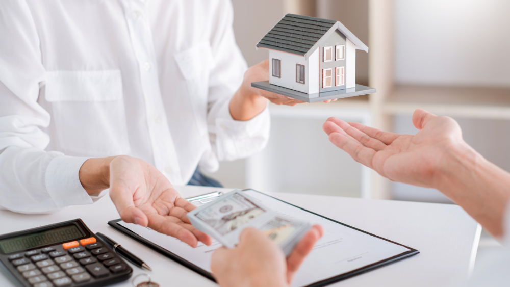 A woman is holding a model house and giving money to another woman.