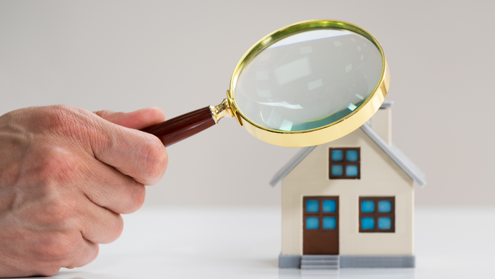 A person is holding a magnifying glass over a model house.