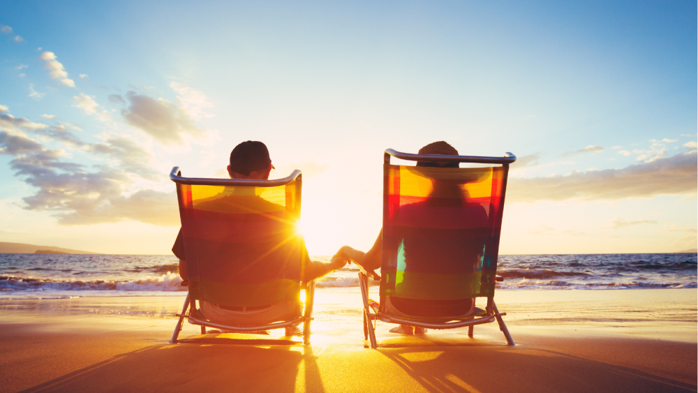 A man and a woman are sitting in beach chairs on the beach holding hands.