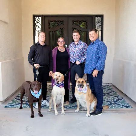 Family of five, three dogs and two adults and two young men in front of a door.