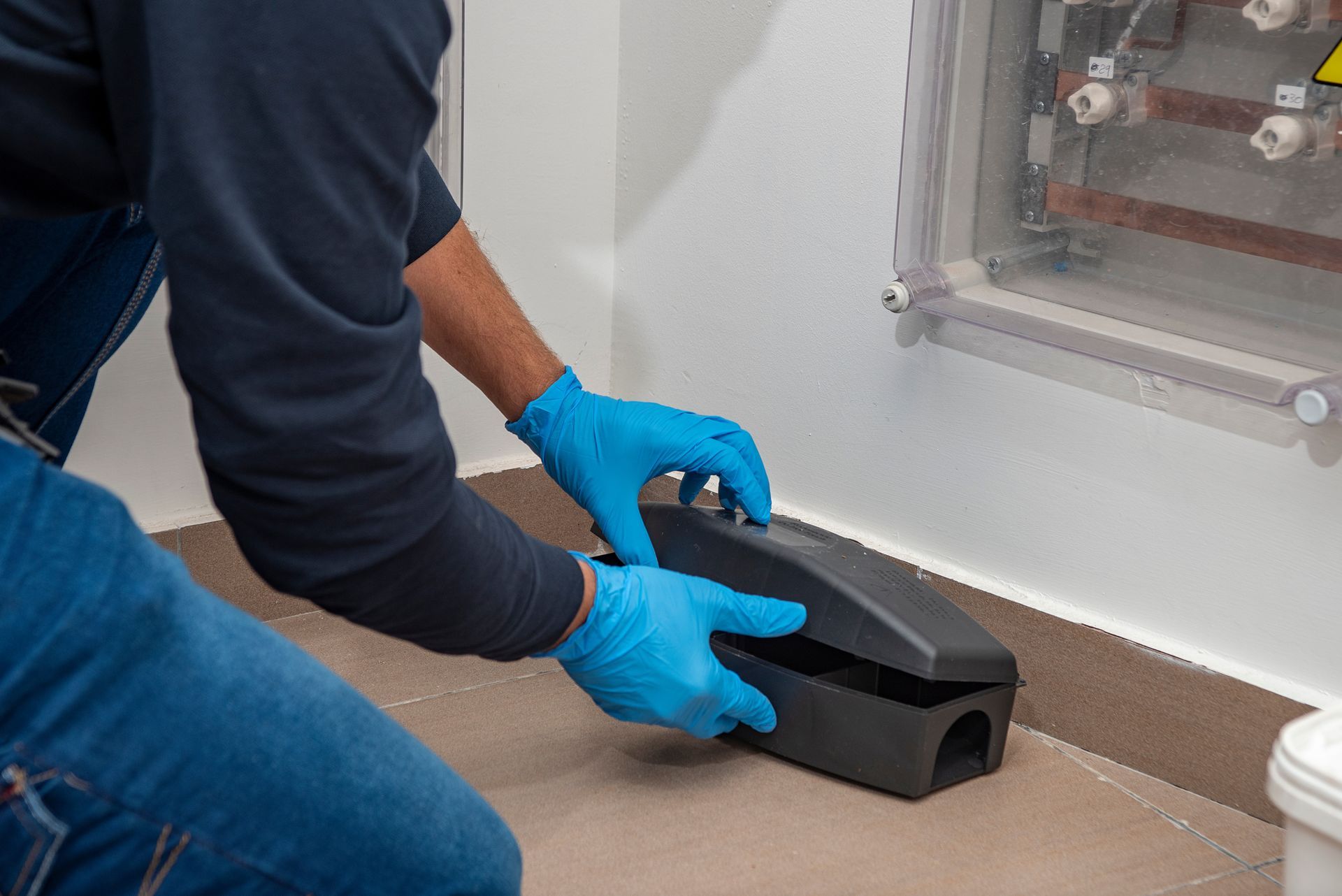 Worker in blue gloves holding a black inspection camera on a floor near a wall panel.