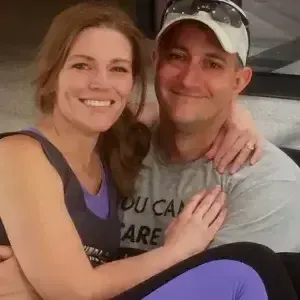 Smiling couple sitting close together indoors, with arms around each other.