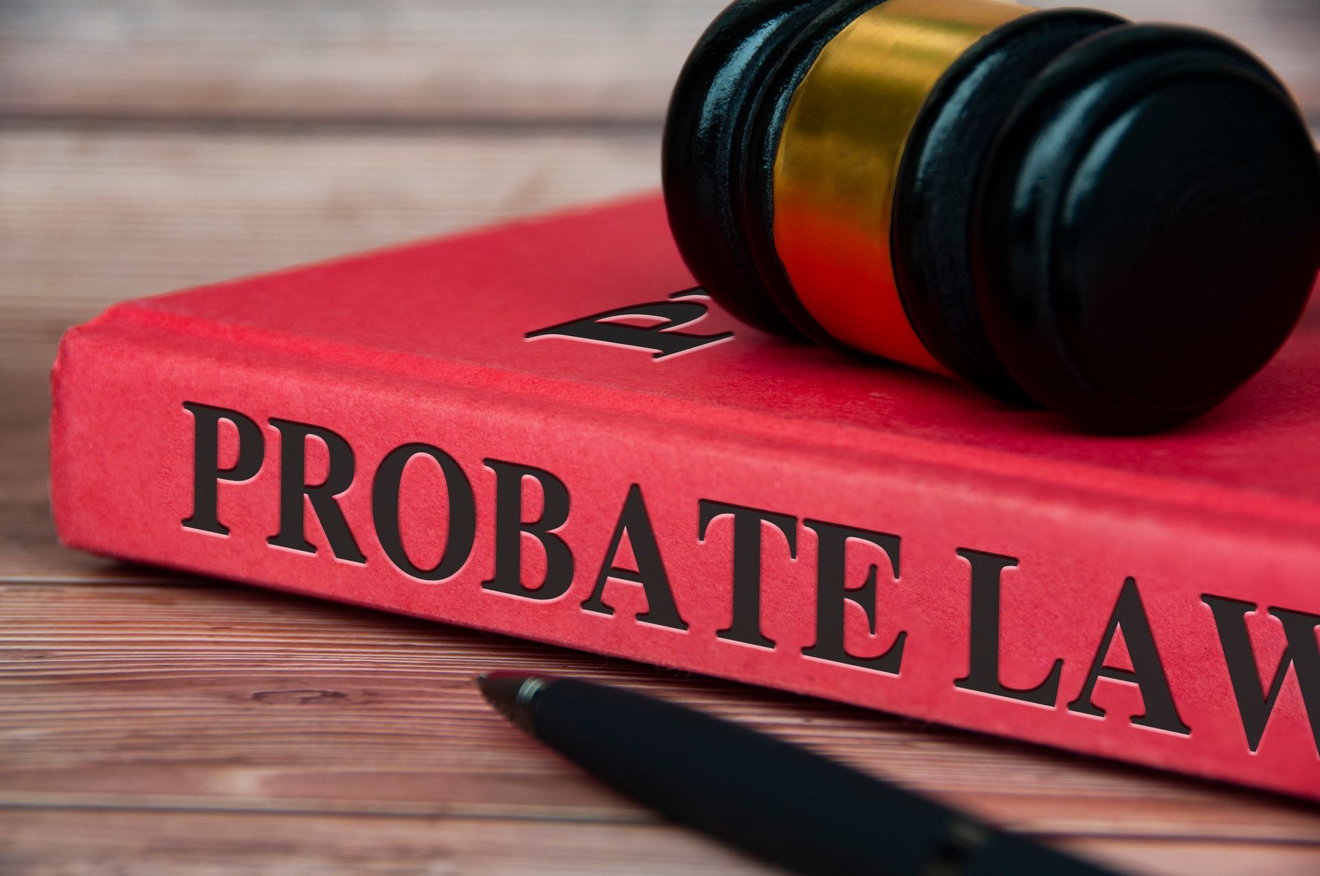 Red  PROBATE LAW  book with gavel on top, and pen at the bottom, on a wooden surface.