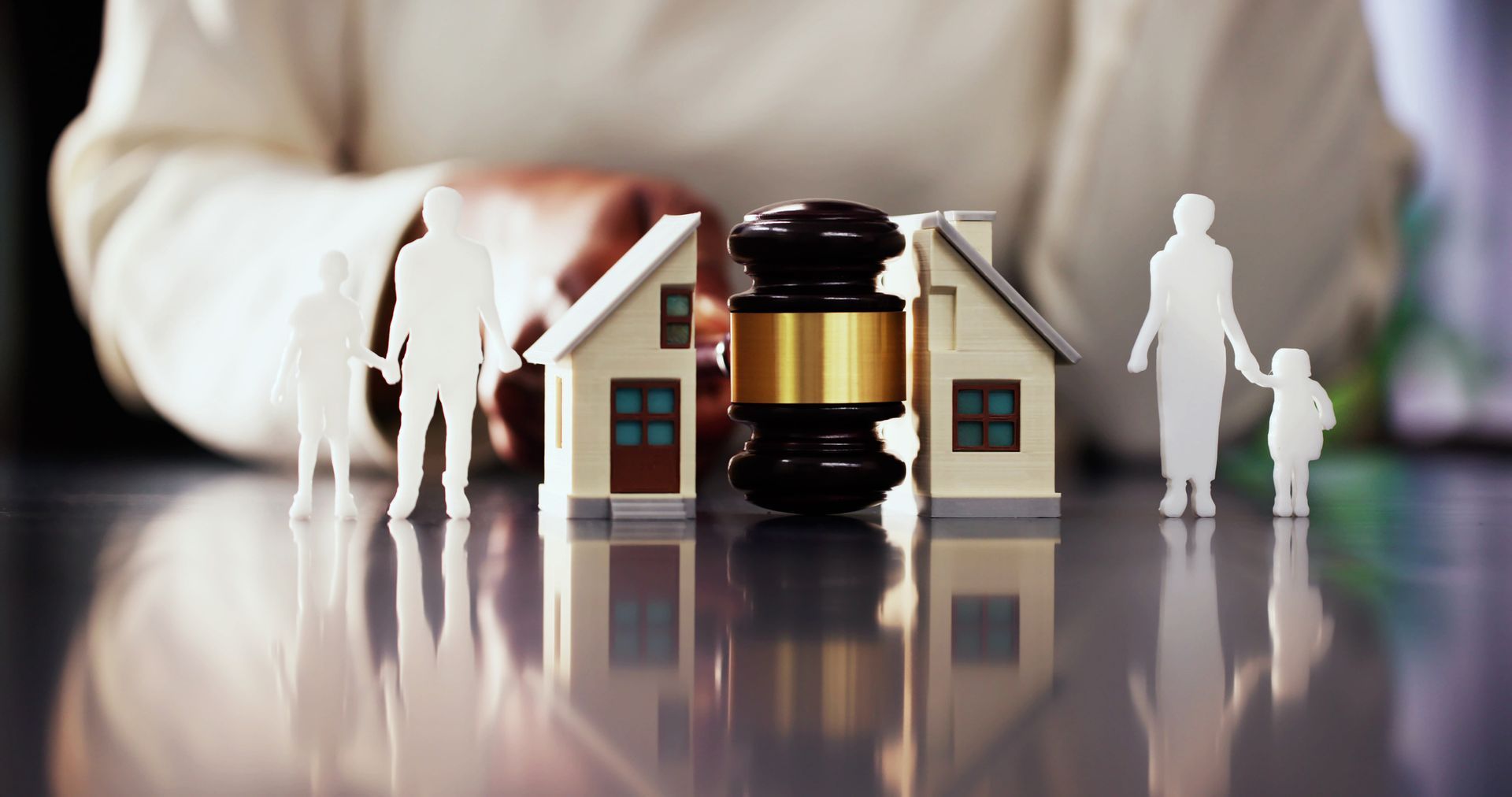 Divorce concept: Gavel between two model houses, family figures on either side.