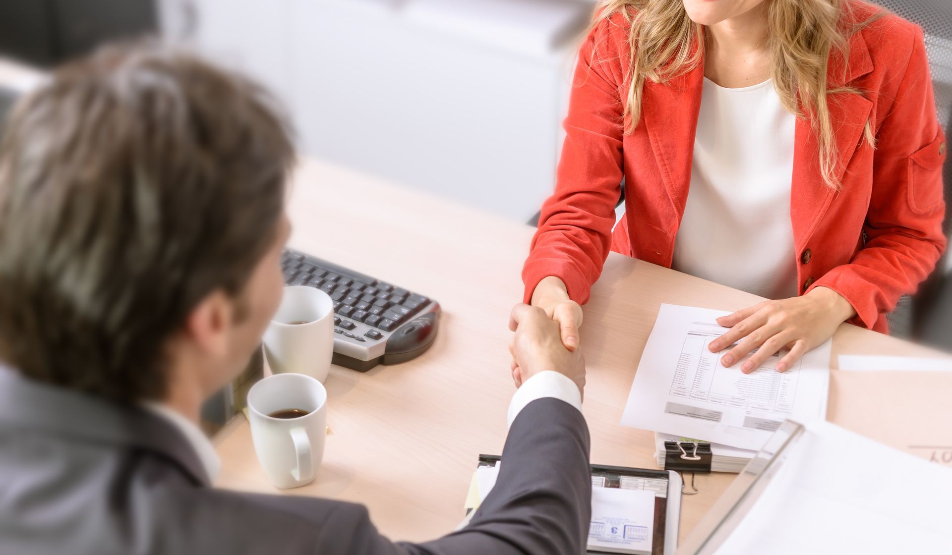Man and woman shaking hands across a desk; financial document visible.