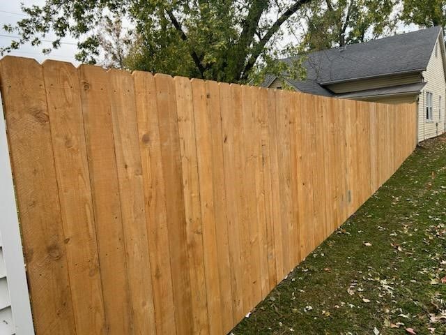 A wooden fence is sitting in the grass next to a house | Ellisville, MO | Americas fence & Deck Com