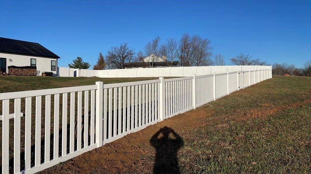 A white picket fence surrounds a grassy field in front of a house. | Warrenton, MO | Americas fence 