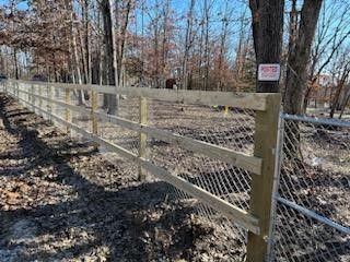 A wooden fence is surrounded by trees and a chain link fence.