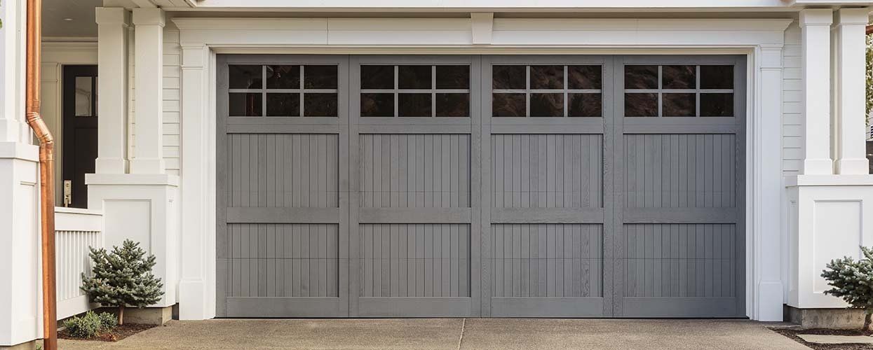 A gray garage door is sitting in front of a white house.