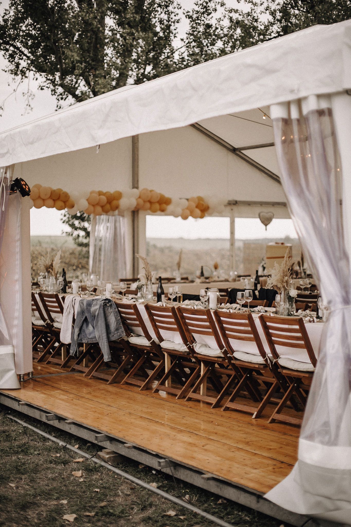 Eine Reihe von Klappstühlen aus Holz unter einem weißen Zelt.