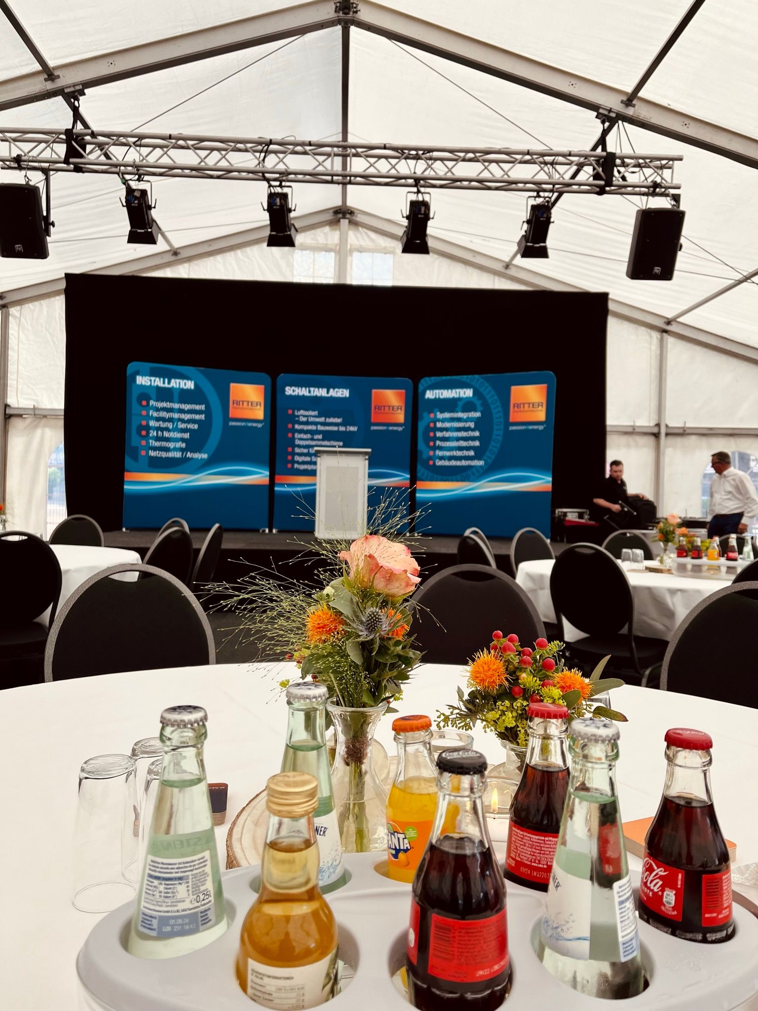 Ein Tisch mit Limonadenflaschen und Blumen darauf in einem Zelt.