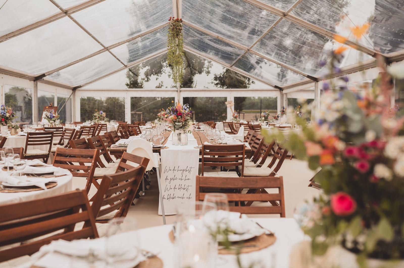 Ein durchsichtiges Zelt mit Tischen und Stühlen für einen Hochzeitsempfang.