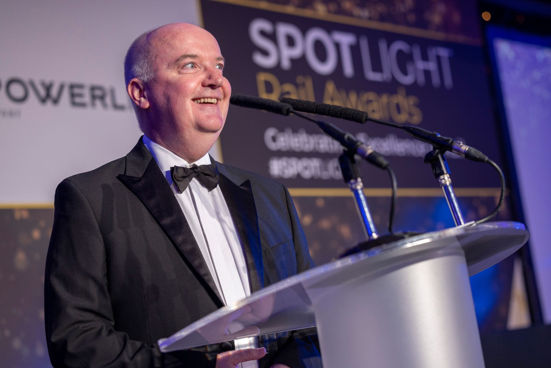 A man in a tuxedo is standing at a podium giving a speech.