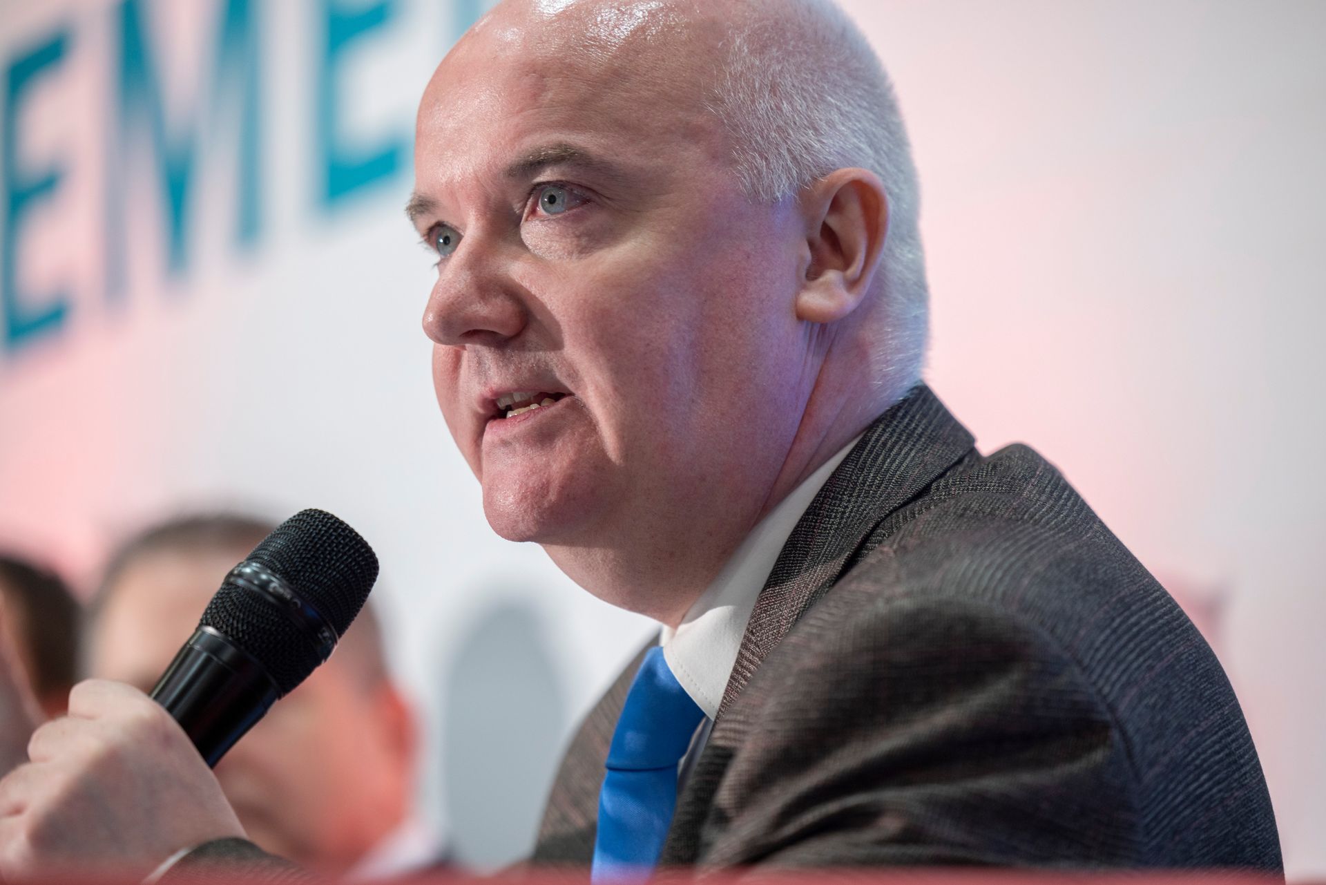 A man in a suit and tie is speaking into a microphone
