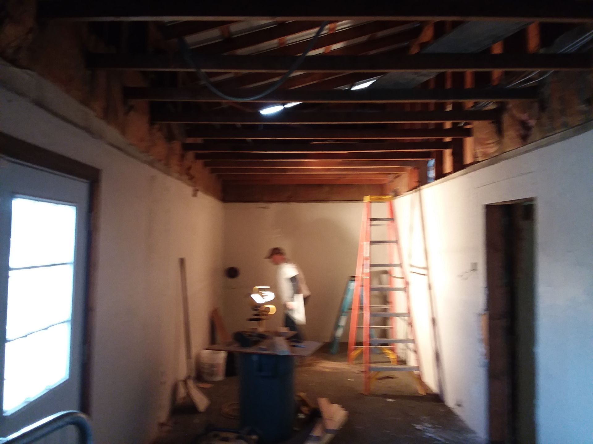 Room under construction with exposed ceiling beams, person working, ladder.