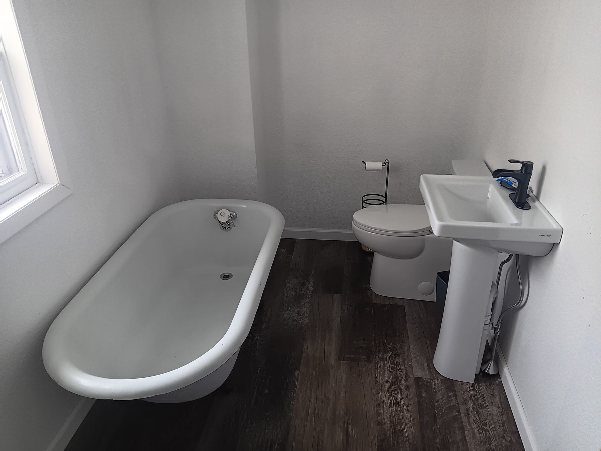 Bathroom with a white clawfoot tub, pedestal sink, and toilet; dark wood-look flooring.
