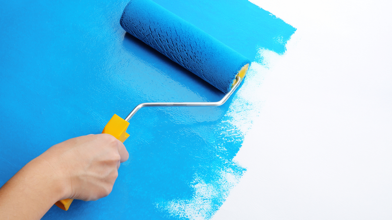 Hand painting a white surface with a blue paint roller.